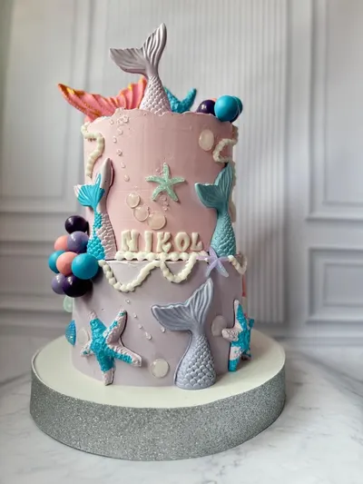Tarta de sirena de dos pisos en rosa y lila con colas de chocolate y estrellas de mar