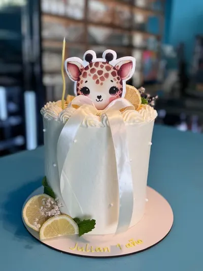 Tarta blanca de primer cumpleaños con una jirafa, lazo de raso y rodajas de limón